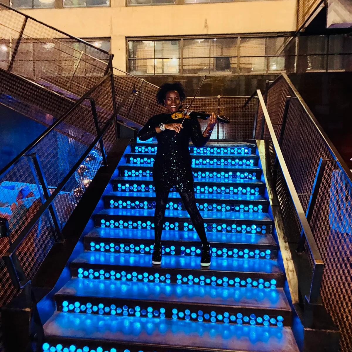 Adia performing violin on a staircase lit with blue lights