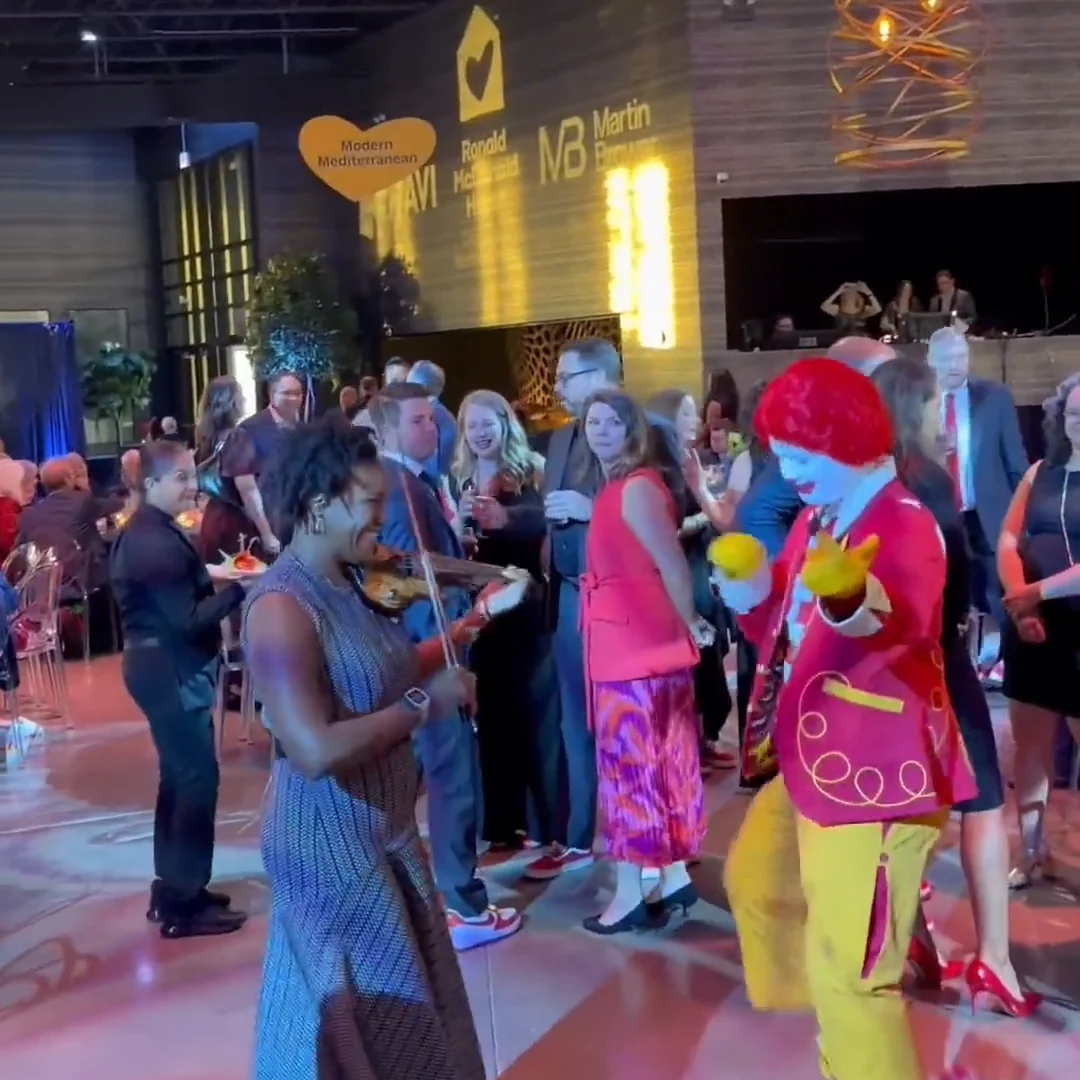 Adia playing violin on the dance floor alongside Ronald McDonald at a Ronald McDonald House Charities gala