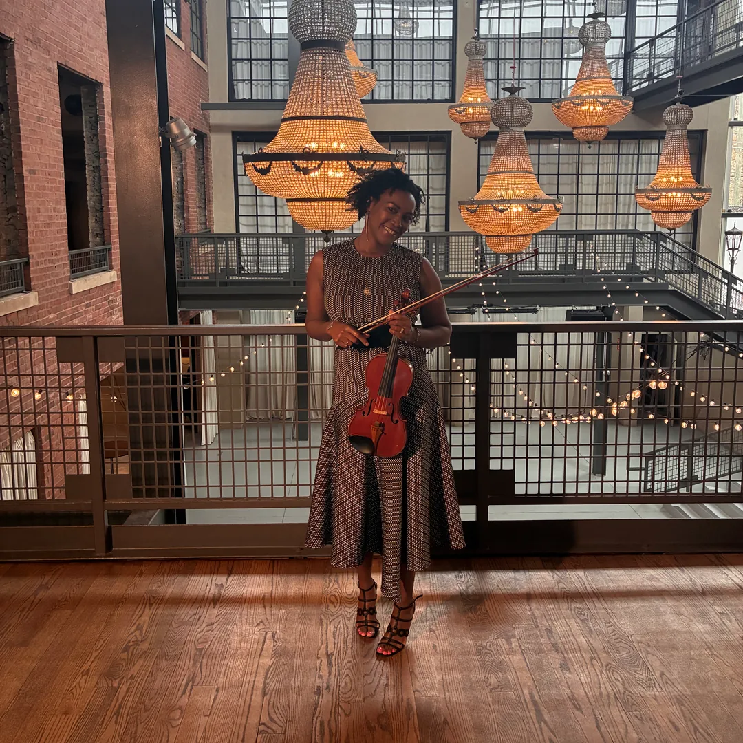Adia playing violin beneath crystal chandeliers in a loft wedding venue