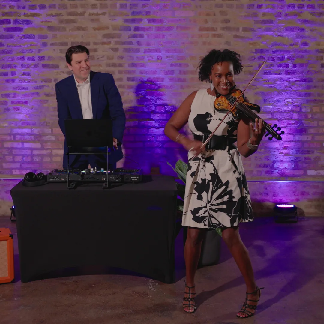 Adia performing electric violin beside her DJ under purple uplighting